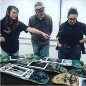 Students in the Photography facility standing behind a table of color photographs.