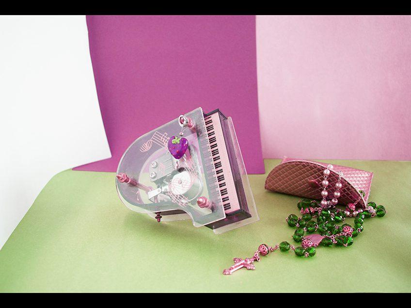 Pastel colored still life with toy piano, beads, and small gold clutch.